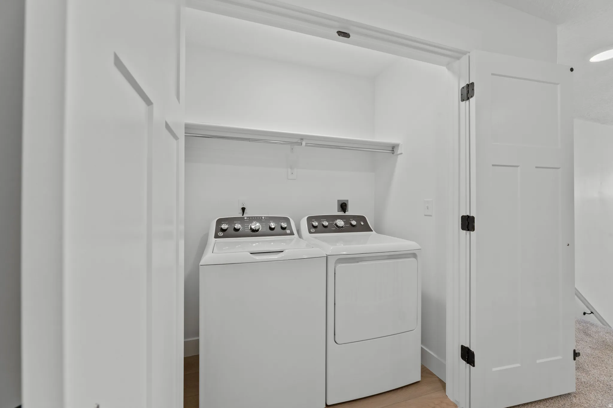 Dedicated laundry closet featuring a washer and dryer, built-in shelving, wood-finish flooring, and white paneled doors with matte black hardware