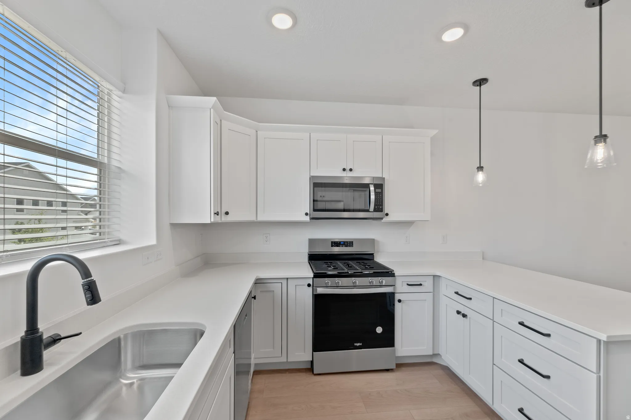 Kitchen featuring white shaker cabinetry, white countertops, stainless steel appliances, a matte black faucet, and pendant lighting
