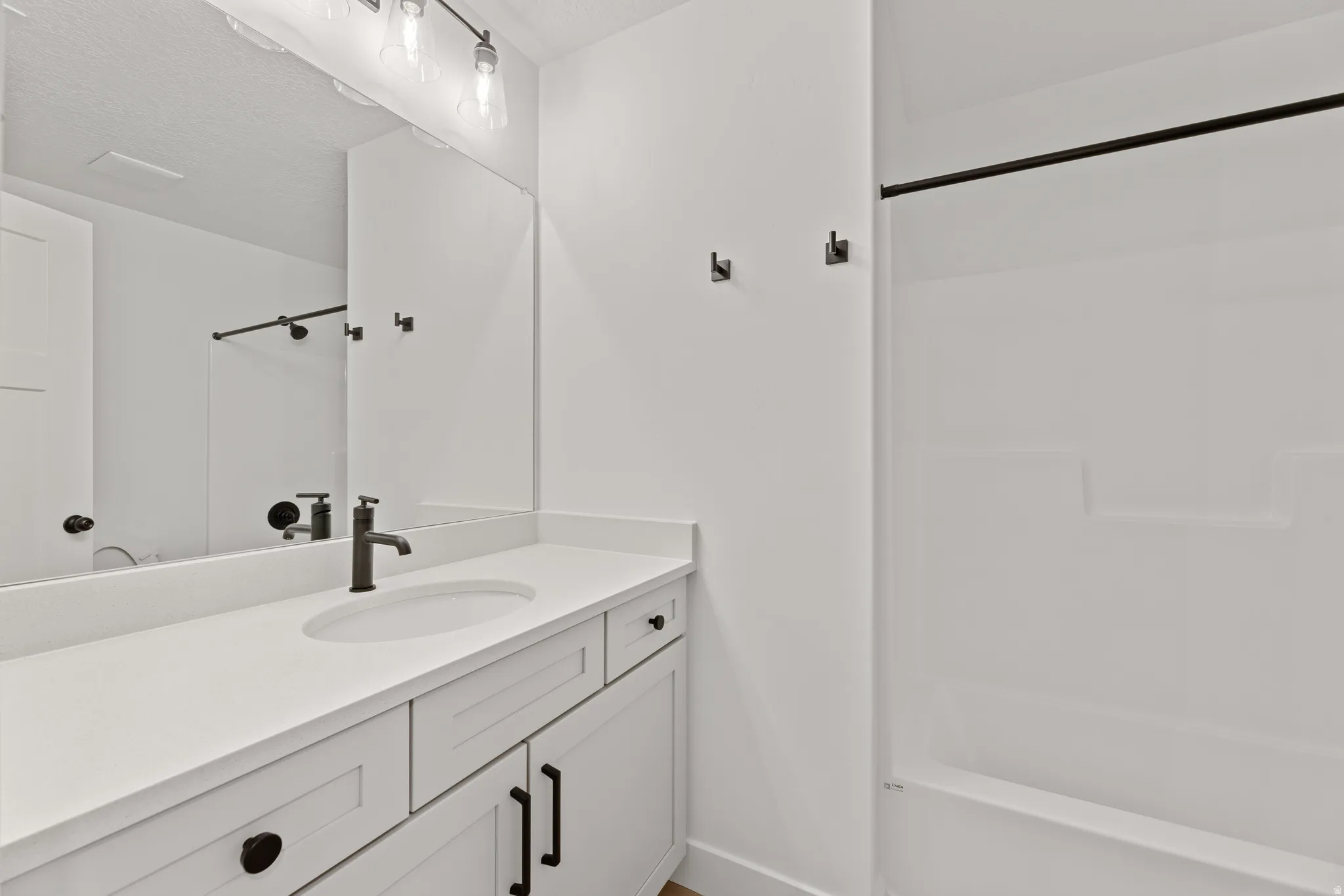 Bathroom featuring a white vanity with integrated sink, a large wall-mounted mirror, brushed black hardware throughout, and a white tub with shower surround