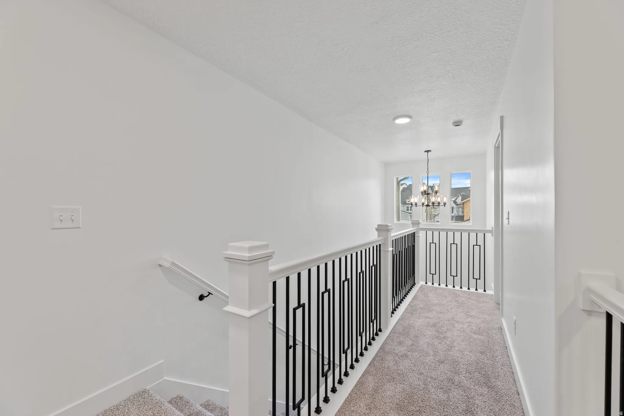 Carpeted hallway featuring white walls, wrought iron railing, and recessed lighting