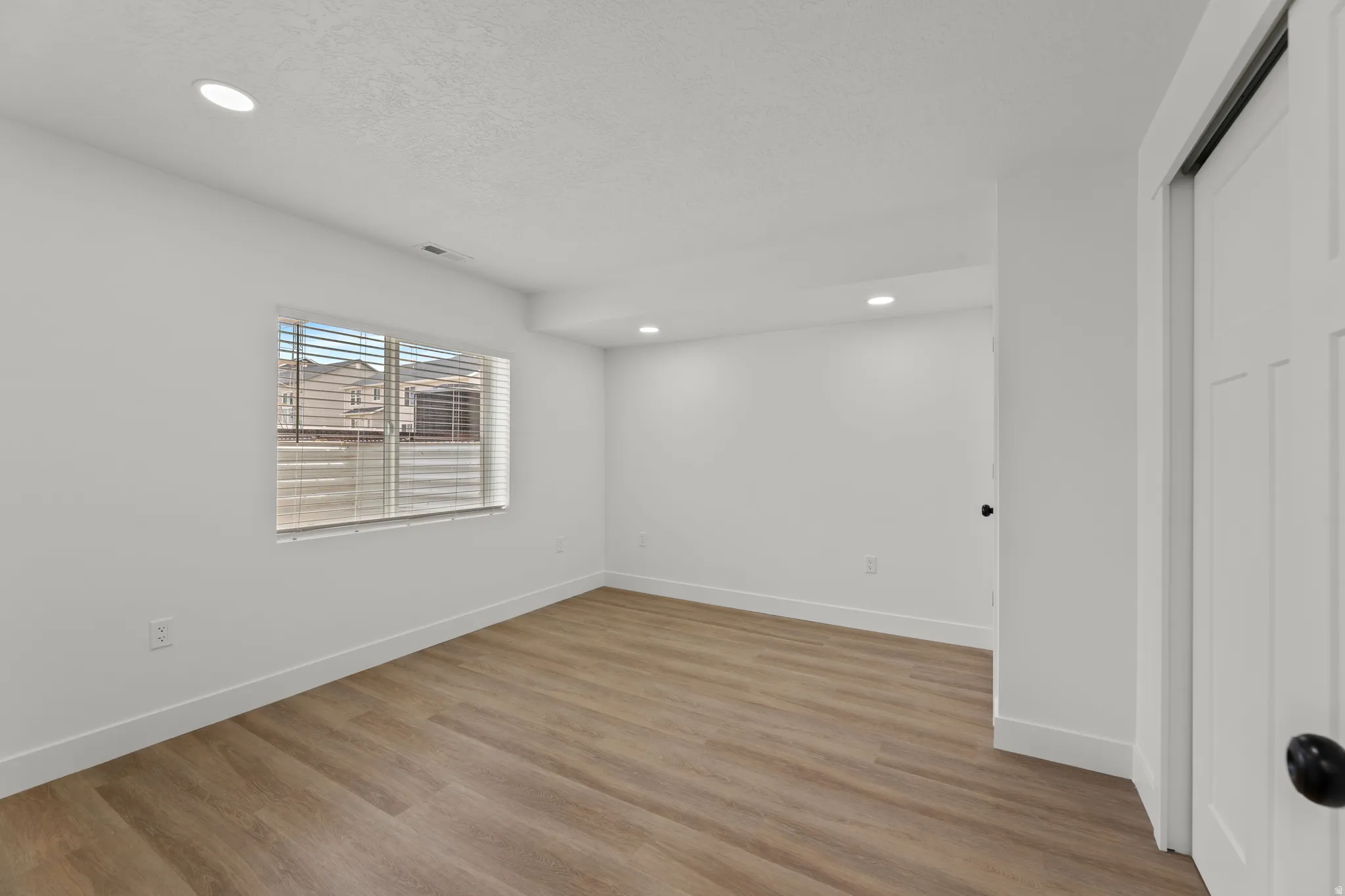 Room featuring wood-finish flooring, recessed ceiling lighting, and a window with horizontal blinds