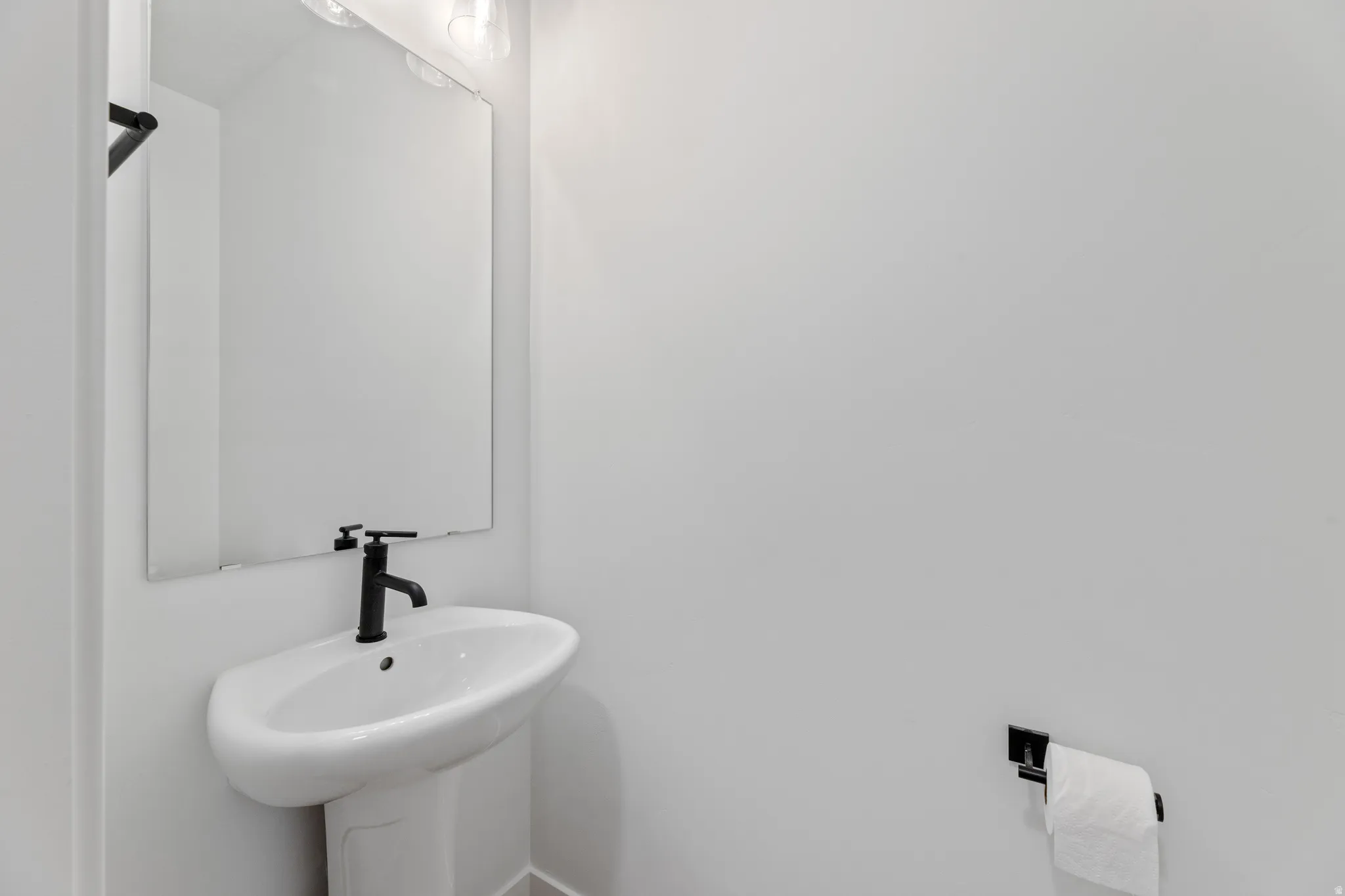 Pedestal sink with matte black faucet, wall-mounted mirror, and overhead vanity lighting
