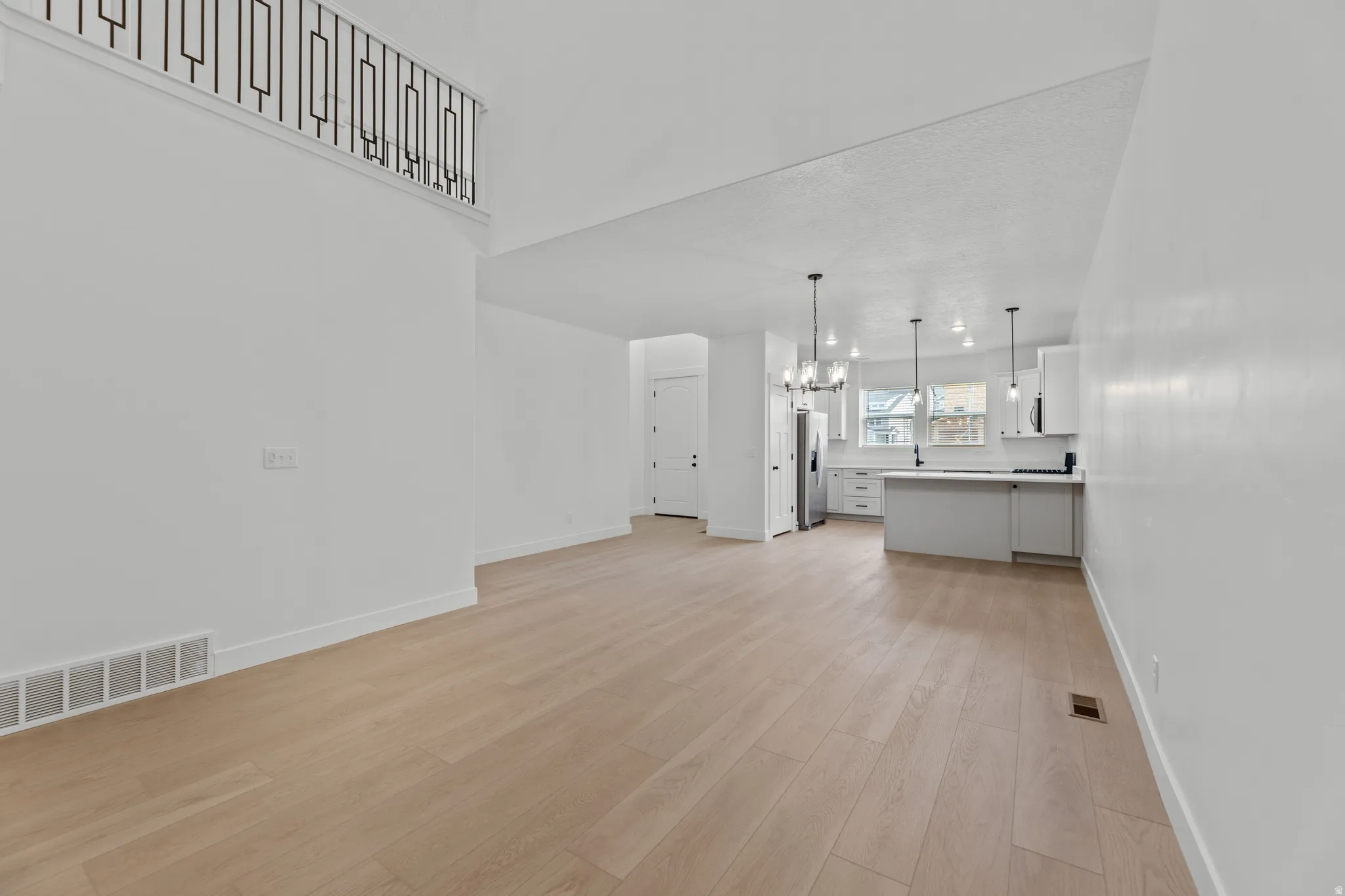 Expansive living area featuring light wood-finish flooring, a two-story ceiling, and a contemporary railing