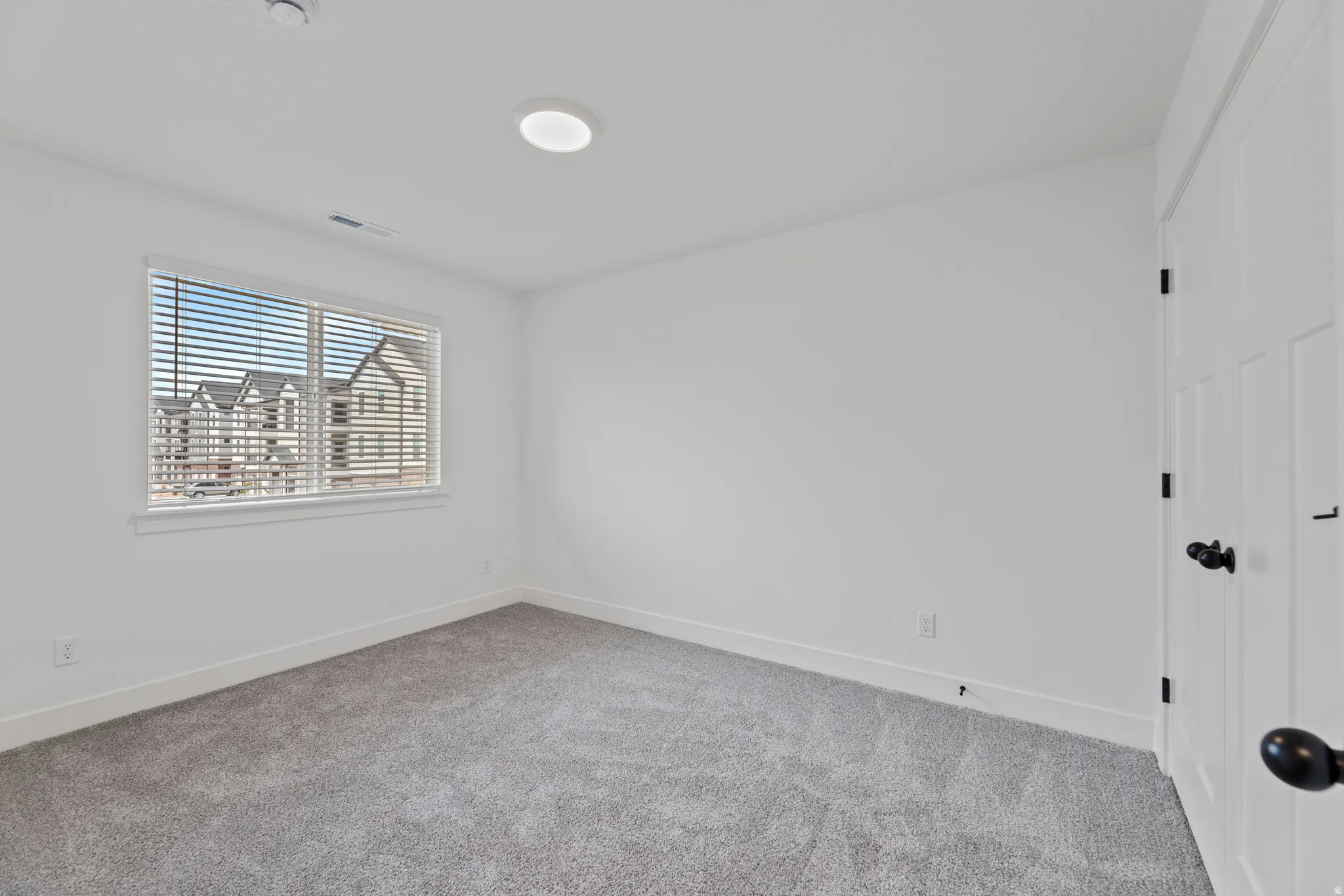Room featuring light gray carpet flooring, white walls, and a window with white blinds