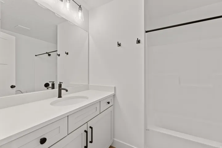Bathroom featuring a white vanity with integrated sink, a large wall-mounted mirror, brushed black hardware throughout, and a white tub with shower surround