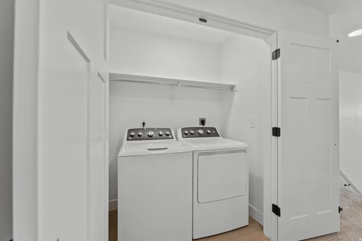 Dedicated laundry closet featuring a washer and dryer, built-in shelving, wood-finish flooring, and white paneled doors with matte black hardware