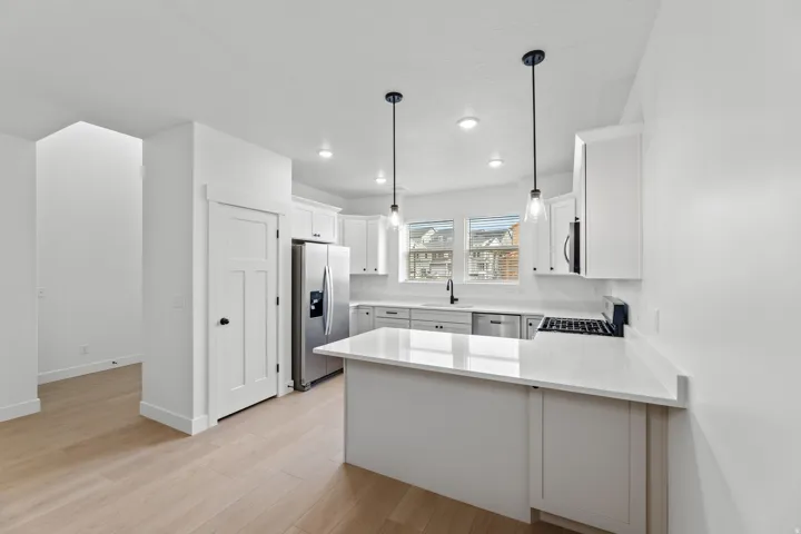 Modern kitchen featuring light wood-finish flooring, white cabinetry, integrated stainless steel appliances, and a gas cooktop