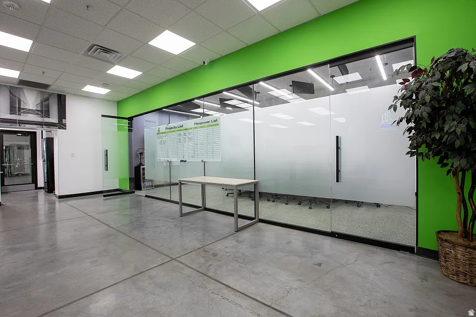 Spacious commercial interior featuring concrete flooring, a dropped acoustic ceiling with integrated square lighting, and a glass partition wall with a frosted lower half