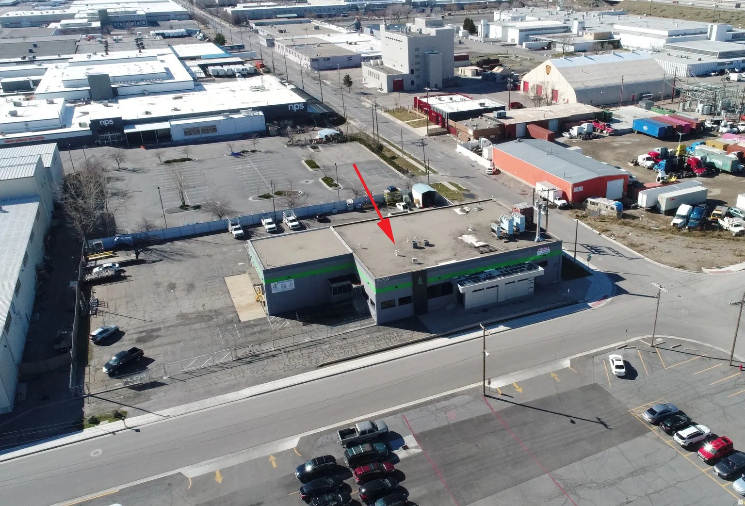 Commercial building featuring a flat roofline, gray and green exterior paneling, and an attached parking lot with designated spaces