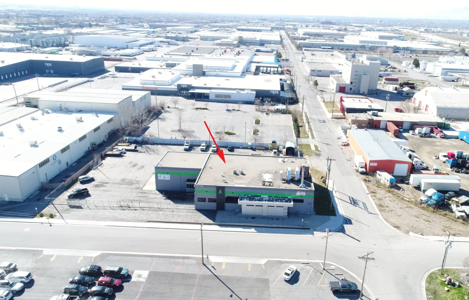 Industrial building featuring a flat roof, green and gray facade, multiple parking spaces, and an accessible corner location
