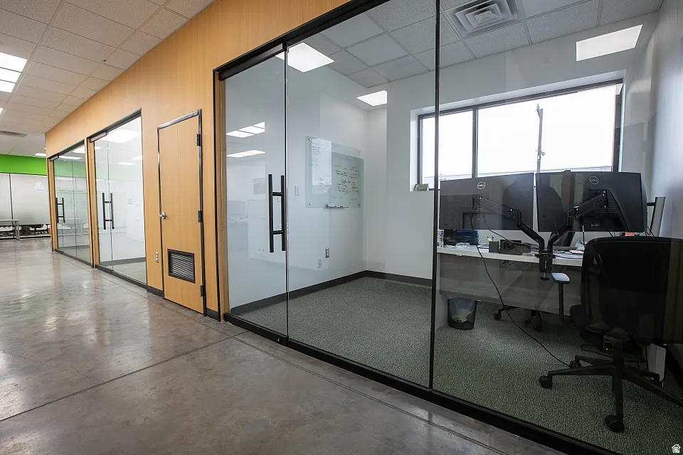 Private office space featuring glass walls with black frames, wood-paneling accents, a large window, recessed lighting, and carpeted flooring