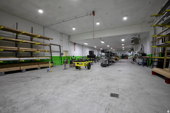 Spacious warehouse interior featuring a concrete floor, high ceilings with recessed lighting, and wall-mounted shelving systems