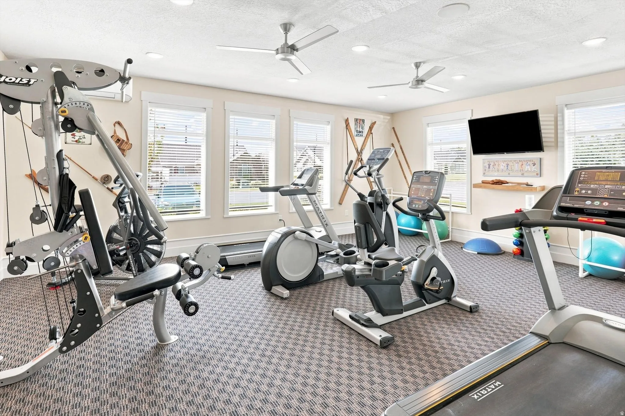 Dedicated fitness room featuring patterned carpet flooring, three large windows with horizontal blinds, and recessed lighting