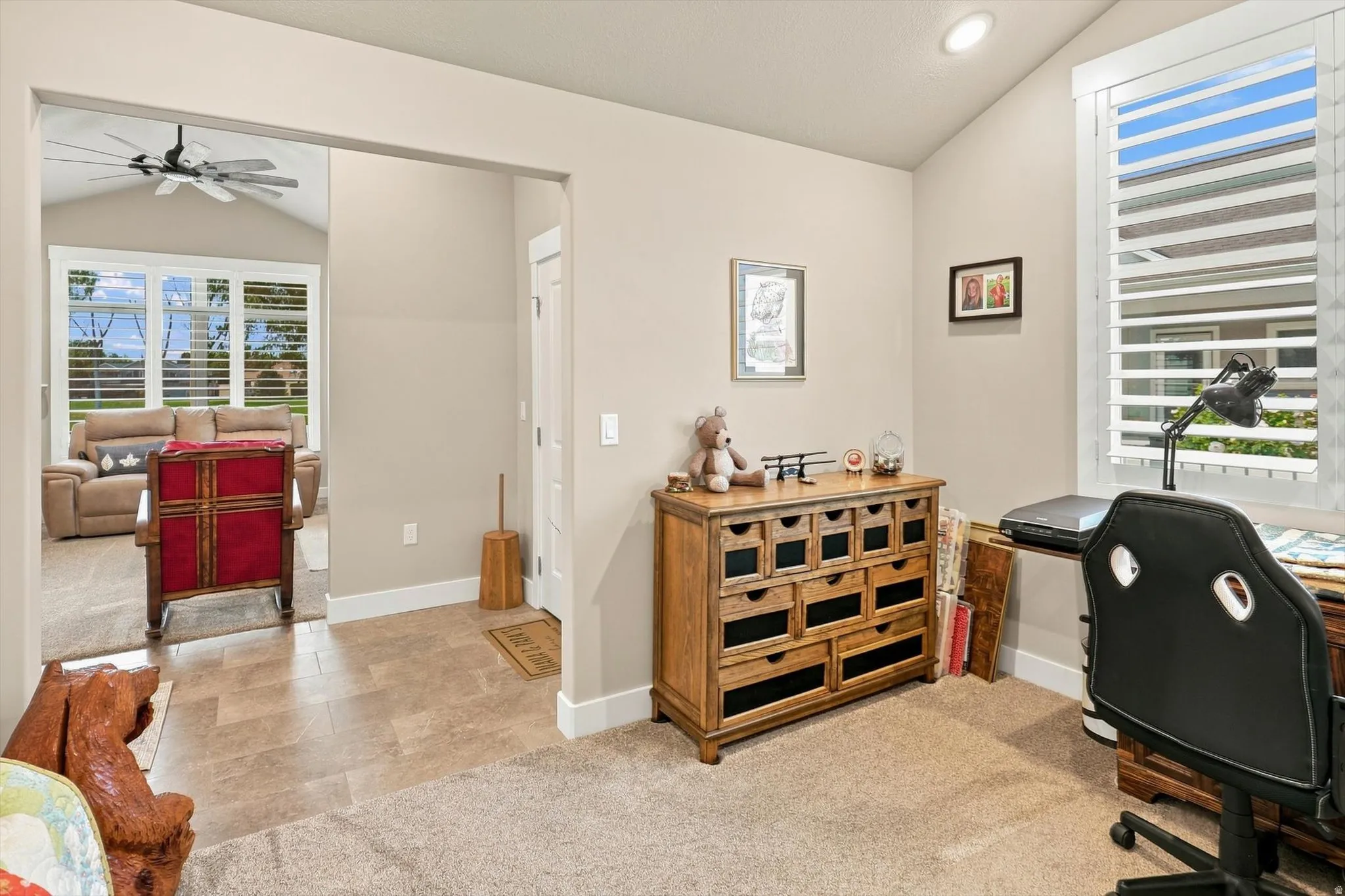 Inviting room featuring a vaulted ceiling and a large window with white plantation shutters