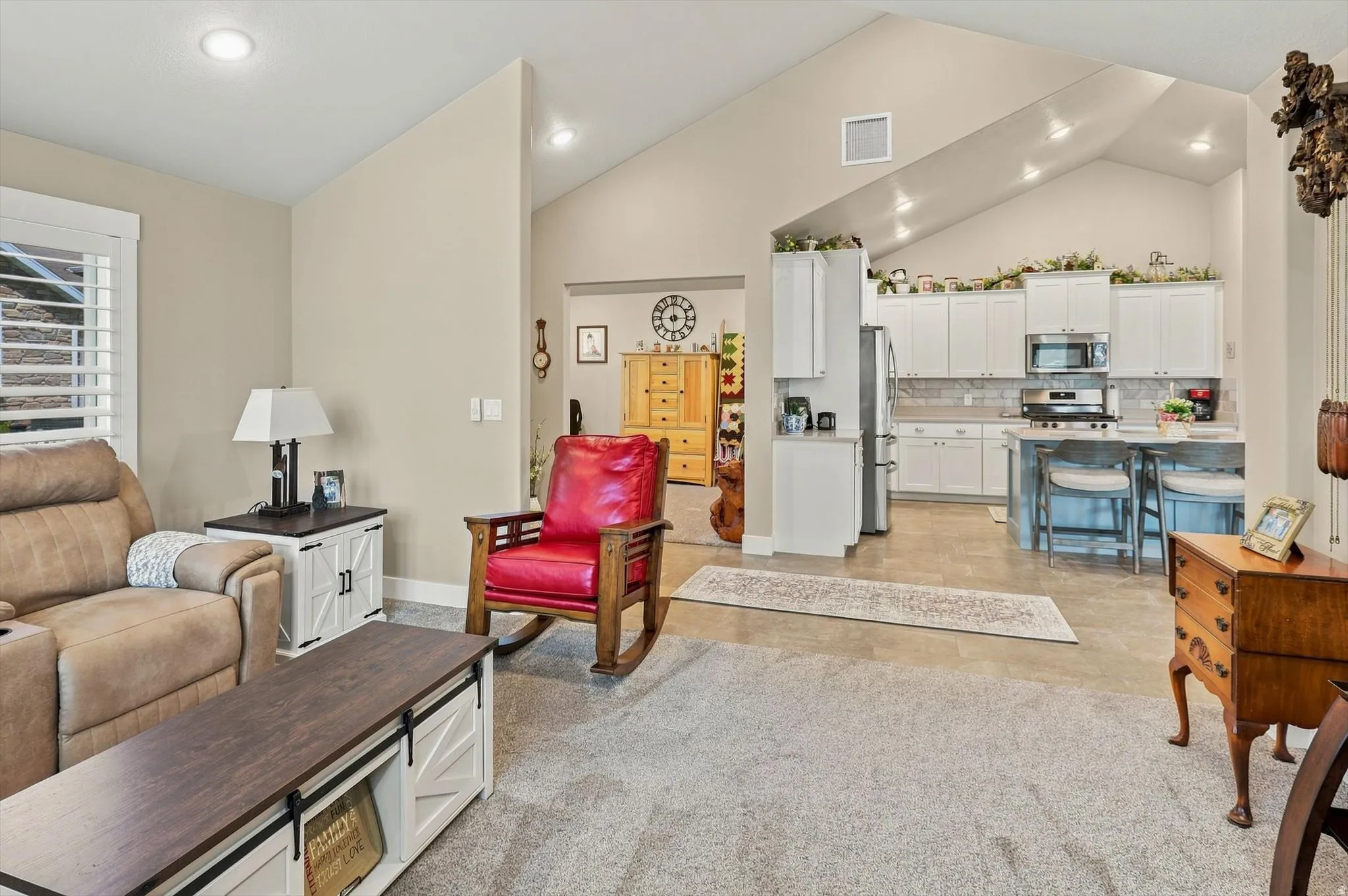 Vaulted ceilings with recessed lighting, an open-concept layout, and a kitchen featuring white cabinetry, stainless steel appliances, and a breakfast bar with built-in seating