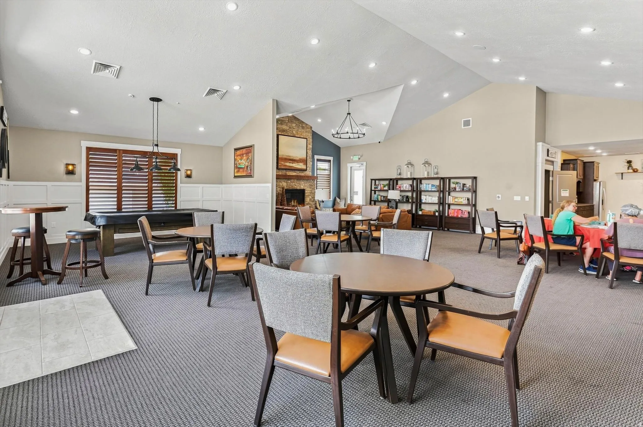 Spacious communal area featuring vaulted ceilings with recessed lighting, carpet flooring, and a stone-clad fireplace
