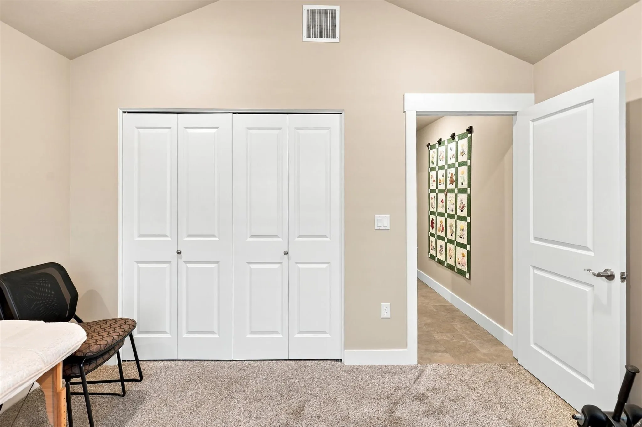 Vaulted ceiling room featuring light beige walls, plush gray carpet flooring, and a double bi-fold closet with white panel doors