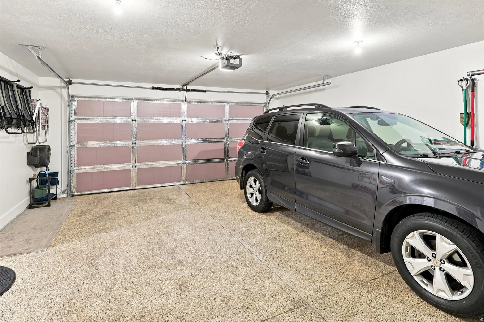 Spacious garage featuring an insulated overhead door, speckled concrete flooring, white painted walls, and overhead lighting