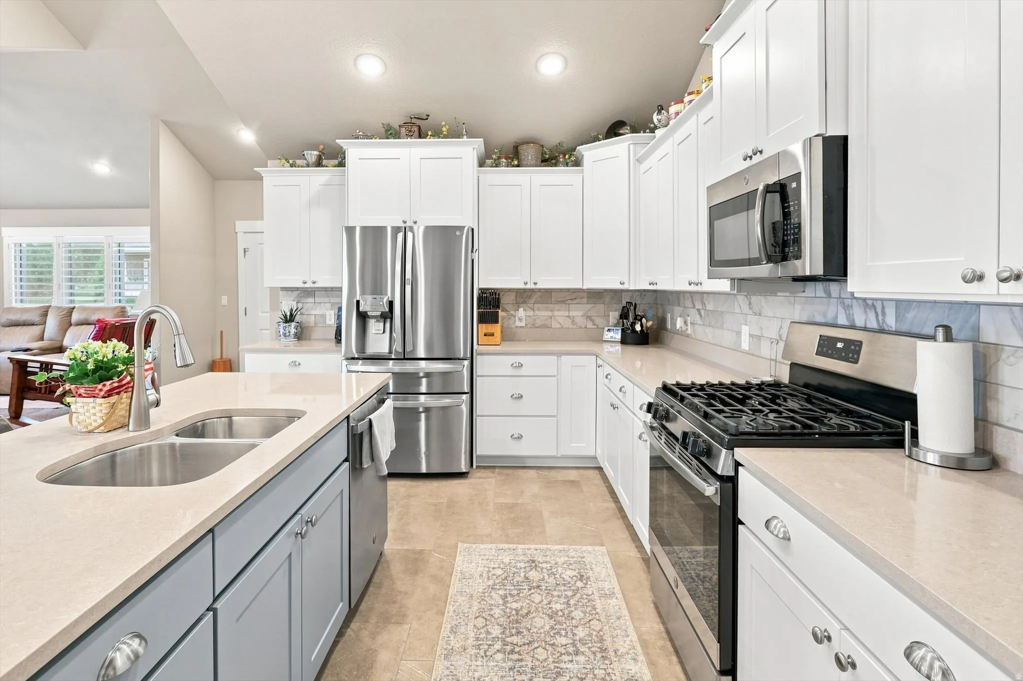 Kitchen featuring light-toned countertops, white upper cabinetry, and a stainless steel appliance suite including a French door refrigerator, microwave, and gas range