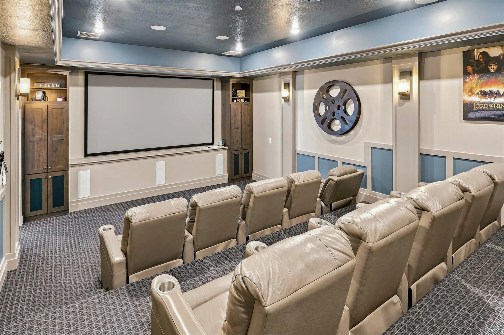 Dedicated home theater featuring a large projection screen, built-in cabinetry, wall sconces, accent lighting, and patterned carpet flooring