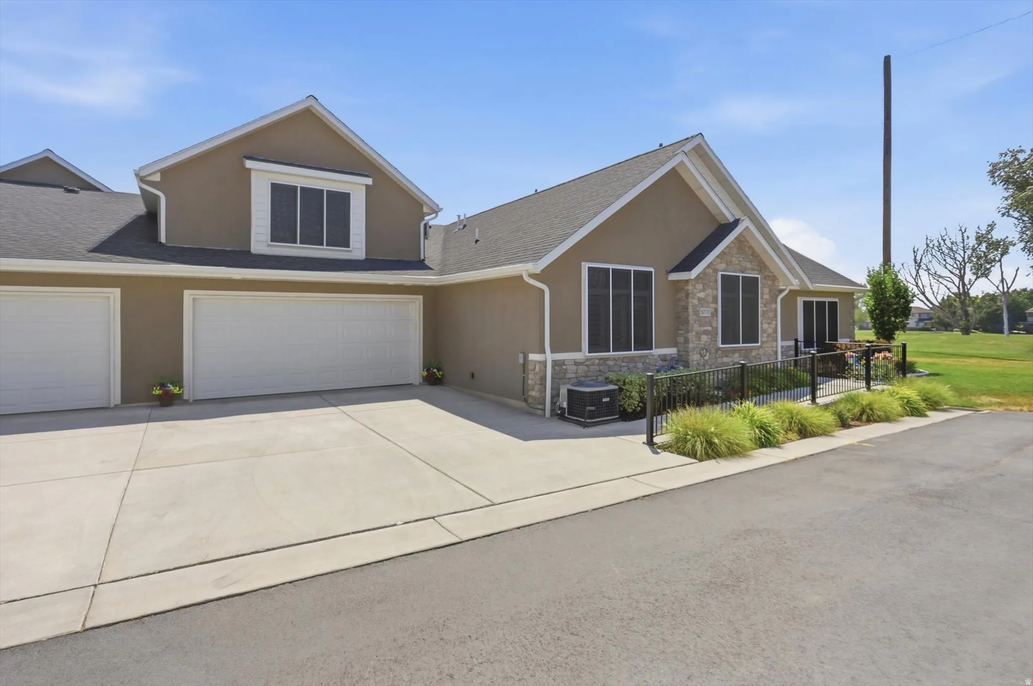 Exterior property featuring stucco siding, stone accents, multiple garage doors, a concrete driveway, and established landscaping