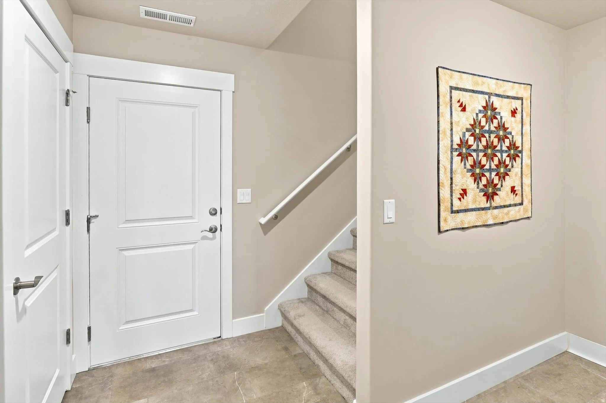 Entryway featuring a white paneled door, gray tiled flooring, a carpeted staircase, and neutral wall tones