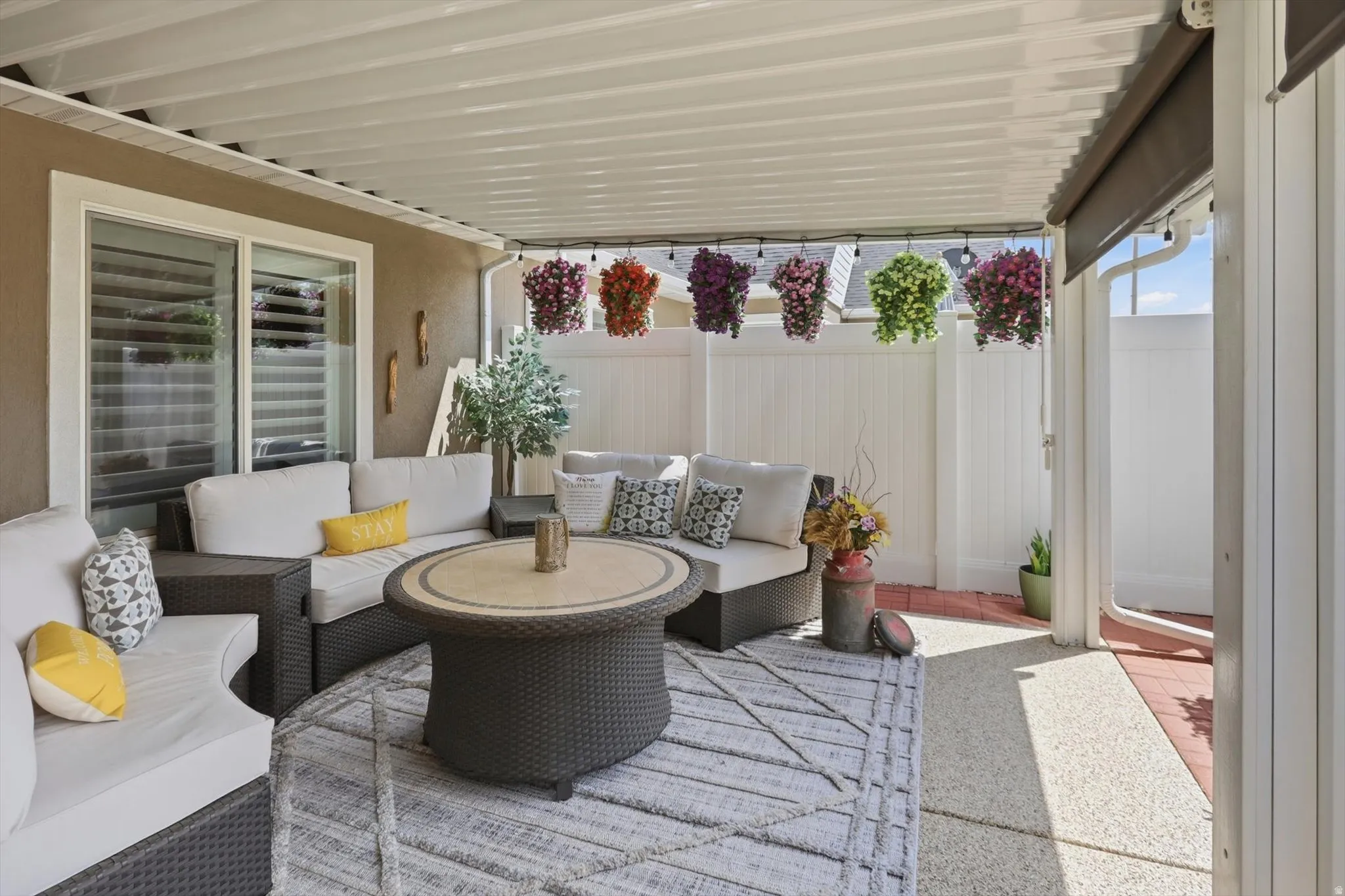 Covered patio featuring a corrugated overhead structure, durable concrete flooring, and a privacy fence