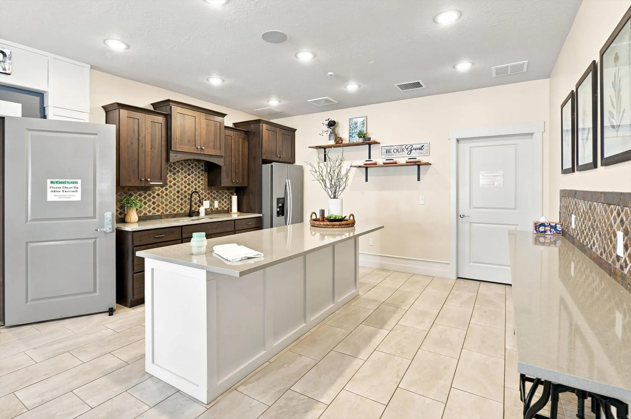 Kitchen featuring a large central island, dark wood-finish cabinetry, a patterned tile backsplash, and light-toned tile flooring