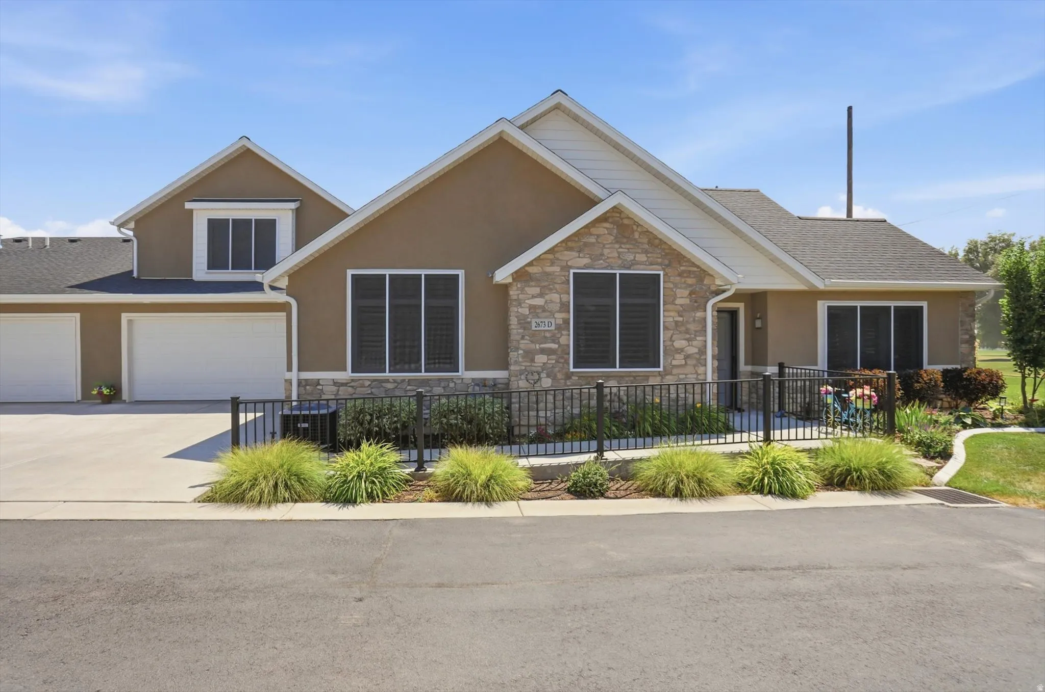 Two-story stucco and stone-clad residence with a multi-car garage, featuring a paved driveway, front-facing windows with dark screens, and a pedestrian ramp leading to the entry