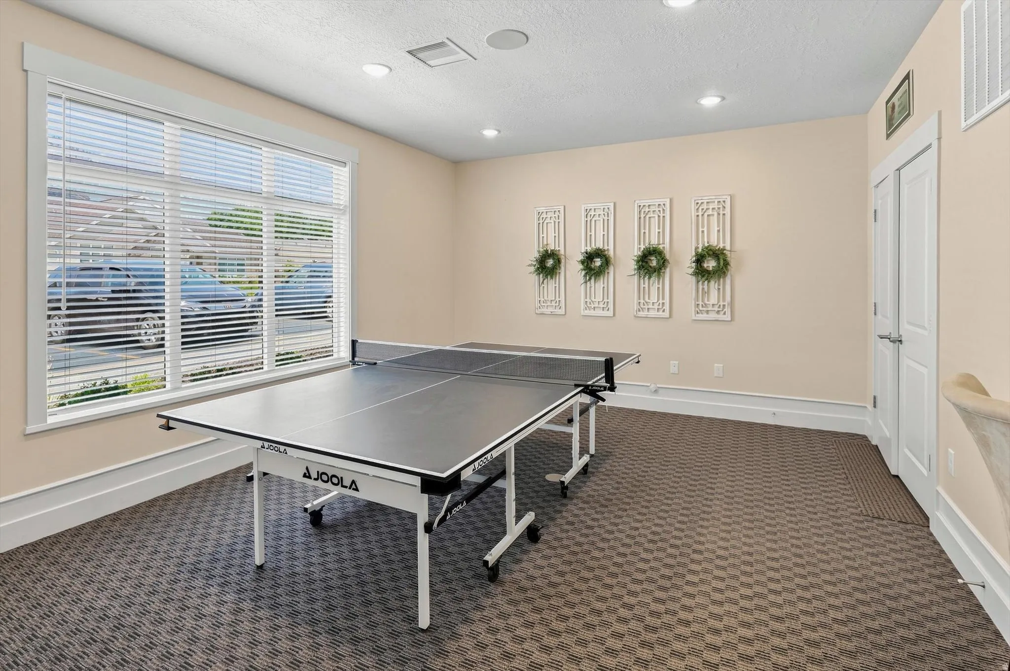 Spacious recreation room featuring large windows with blinds, recessed lighting, and patterned carpet flooring