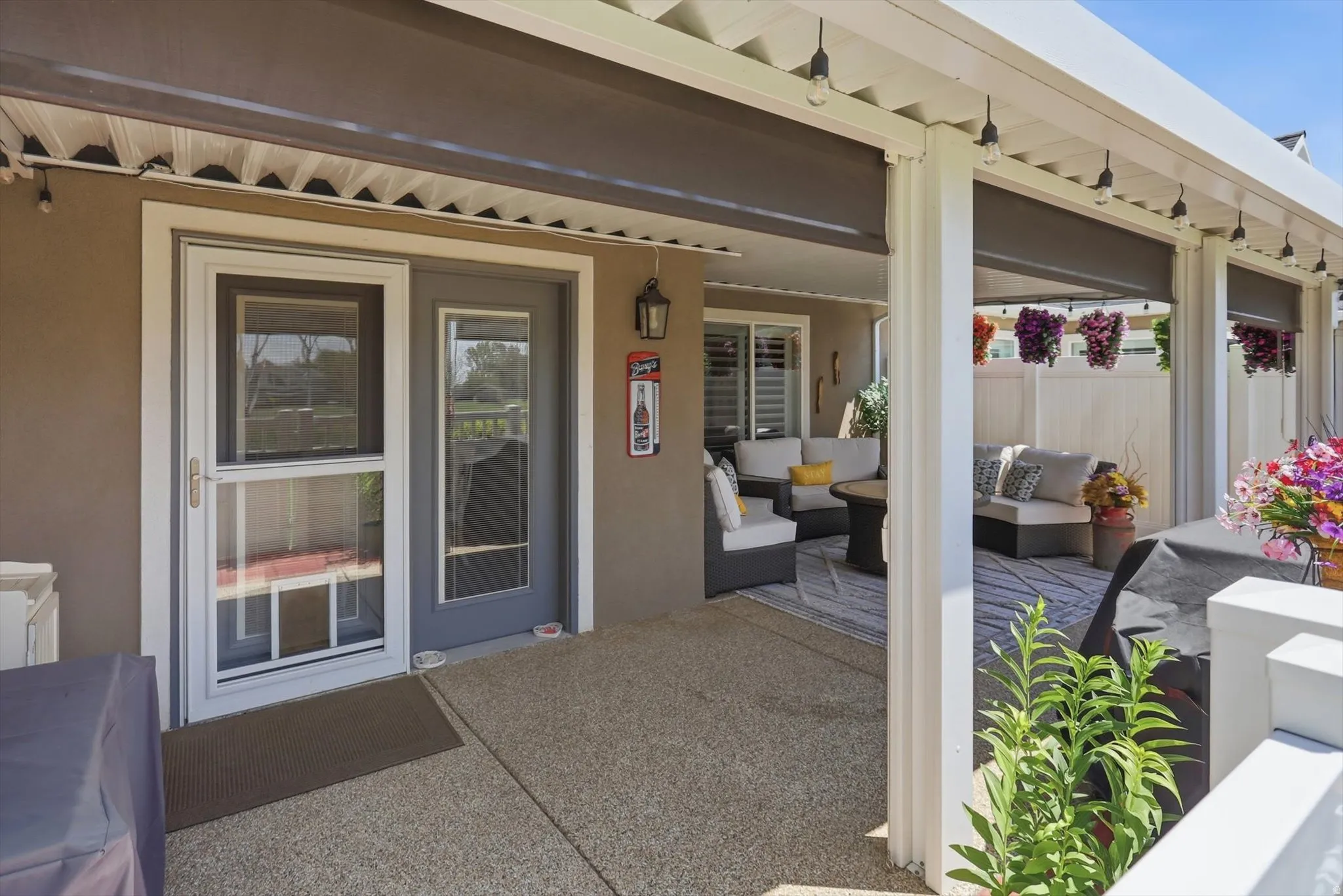 Covered patio featuring an exposed aggregate concrete surface, white columns, and string lighting