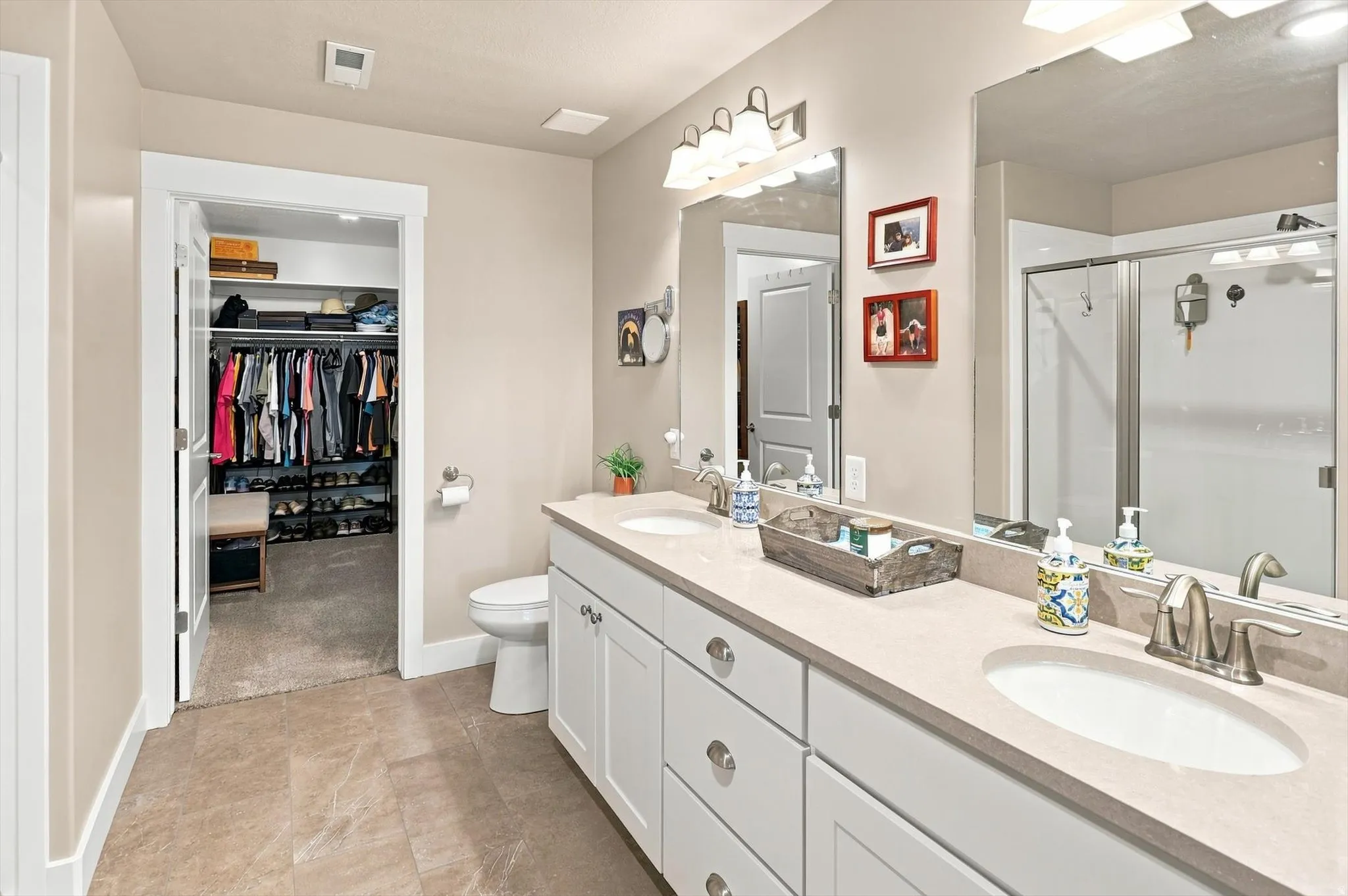 Dual vanity with white cabinetry and light-toned countertops, featuring a separate water closet and an adjacent walk-in closet with built-in shelving