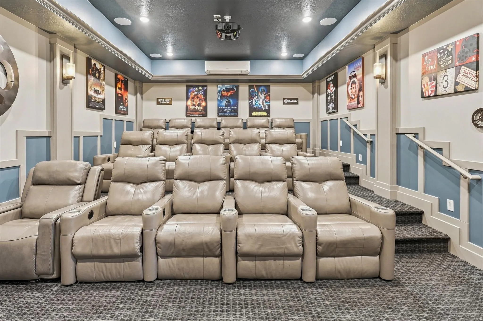 Dedicated media room featuring tiered seating, recessed ceiling lighting, wall sconces, a ceiling-mounted projector, and integrated surround sound speakers