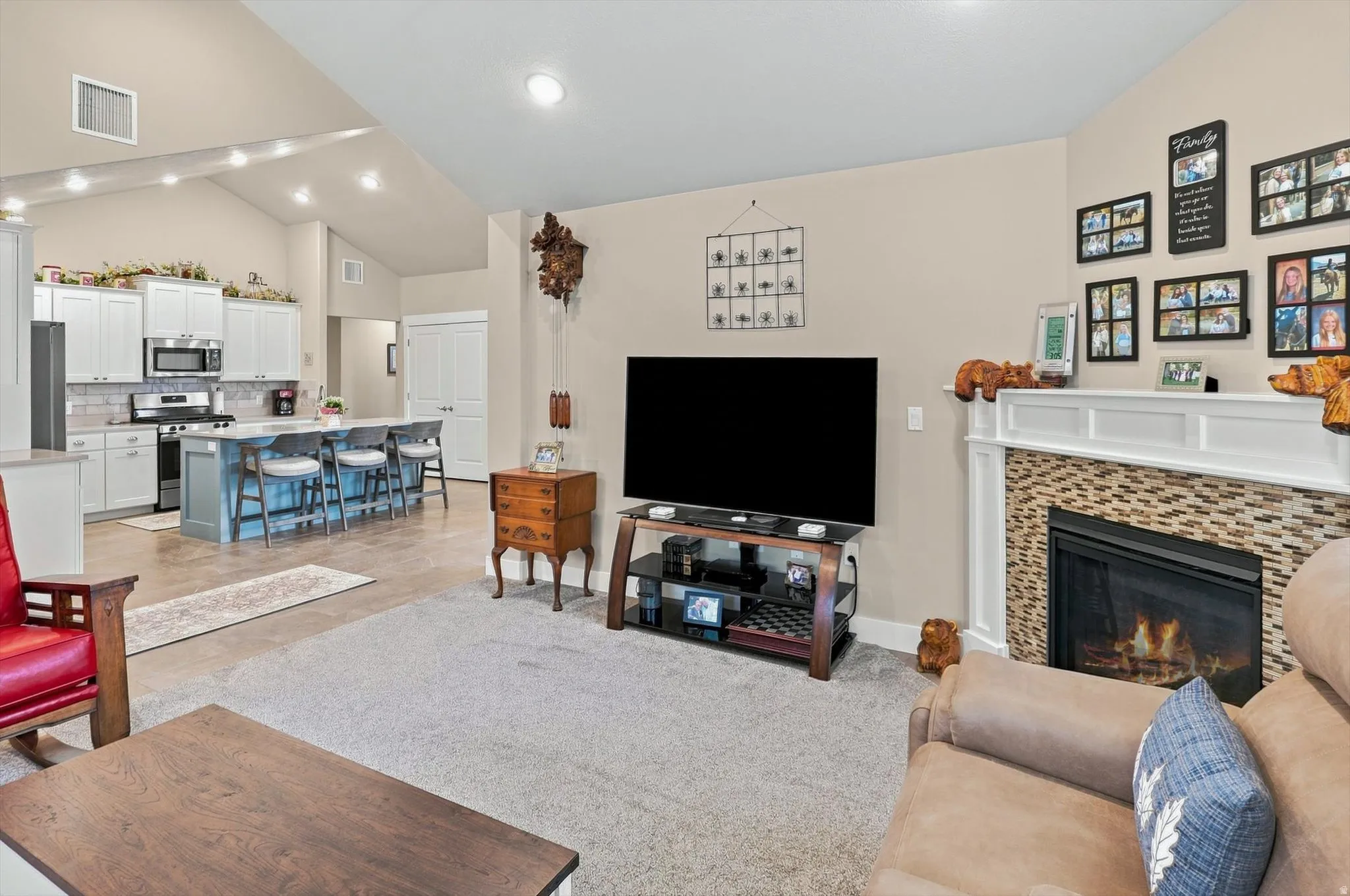 Open-concept living space featuring a fireplace with a decorative tile surround and white mantel, vaulted ceilings, recessed lighting, and wood-finish flooring in the kitchen area