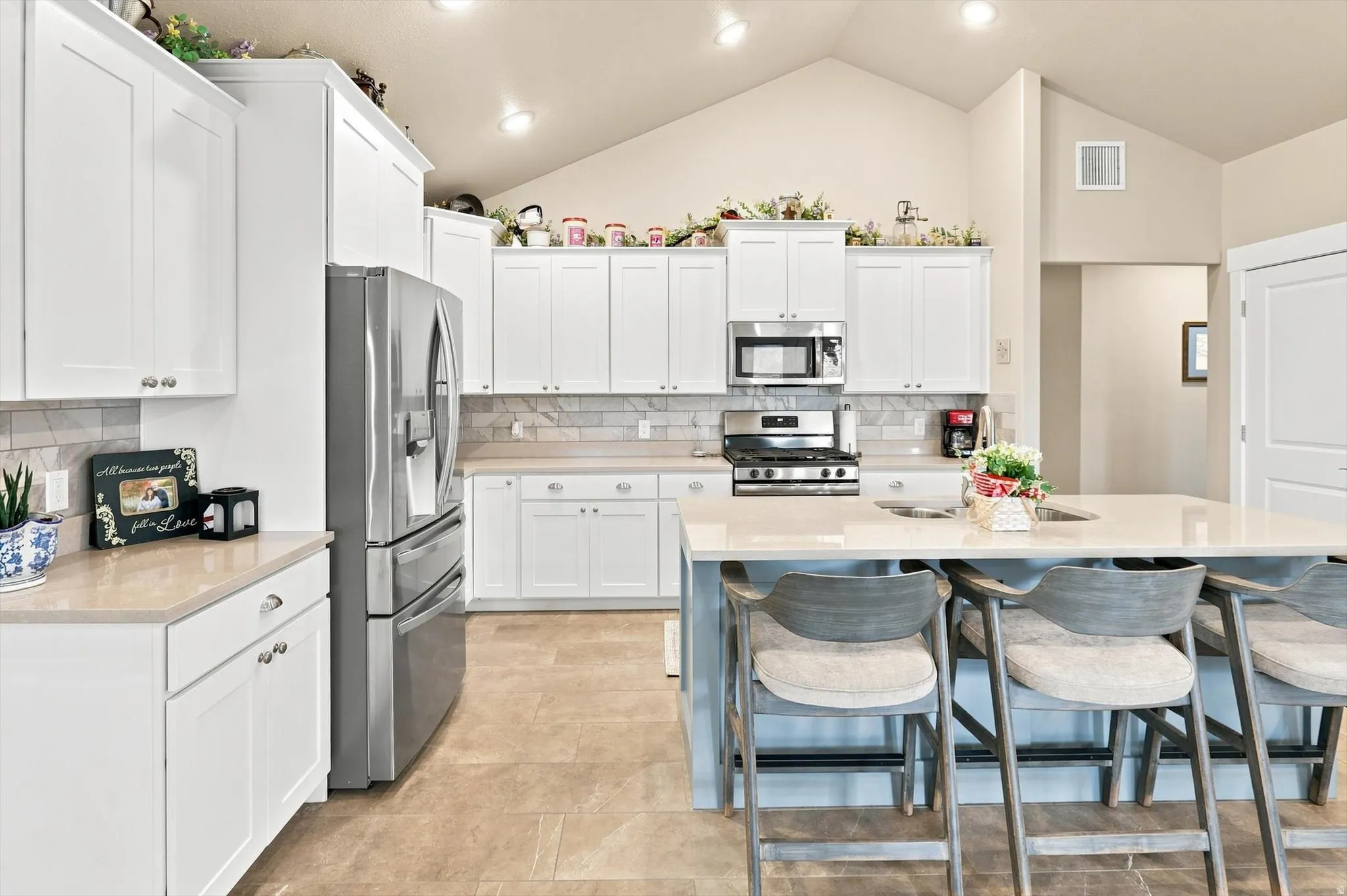 Kitchen featuring a vaulted ceiling with recessed lighting, white cabinetry, stainless steel appliances, a light-toned countertop, and a tile backsplash