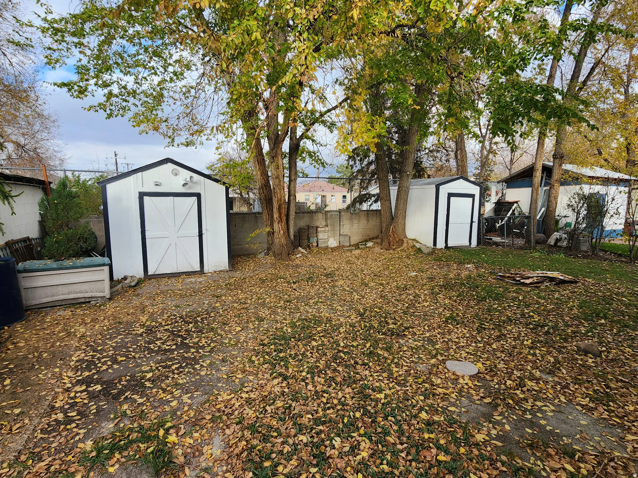 Expansive yard space featuring two white storage sheds with black trim, mature trees, and a concrete block retaining wall