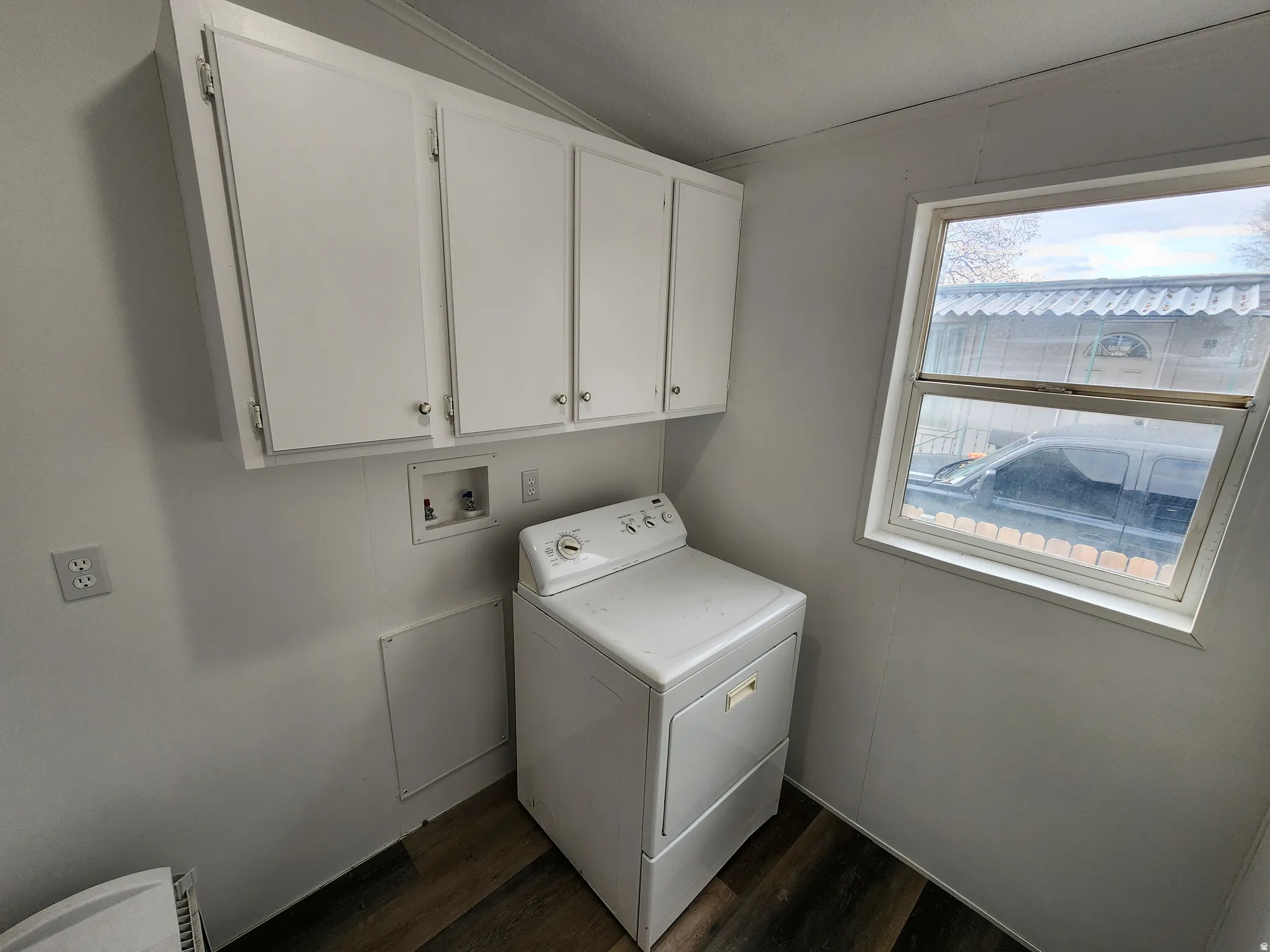 Dedicated laundry area featuring dark wood-finish flooring, white panel walls, and upper cabinetry