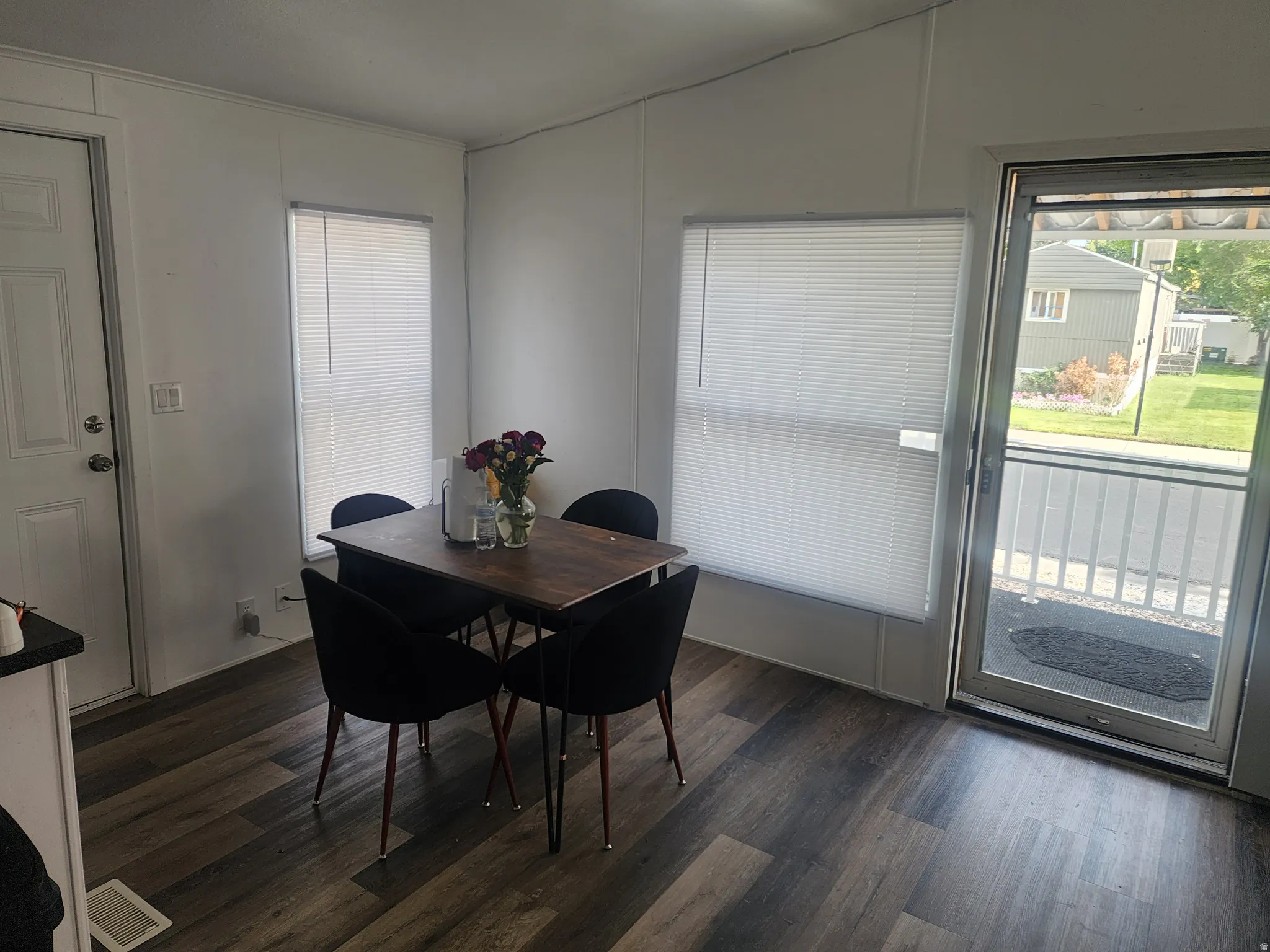 Bright dining area featuring a wood-finish dining table with seating for four, abundant natural light from multiple windows with cellular shades, and sliding glass door access to outdoor space