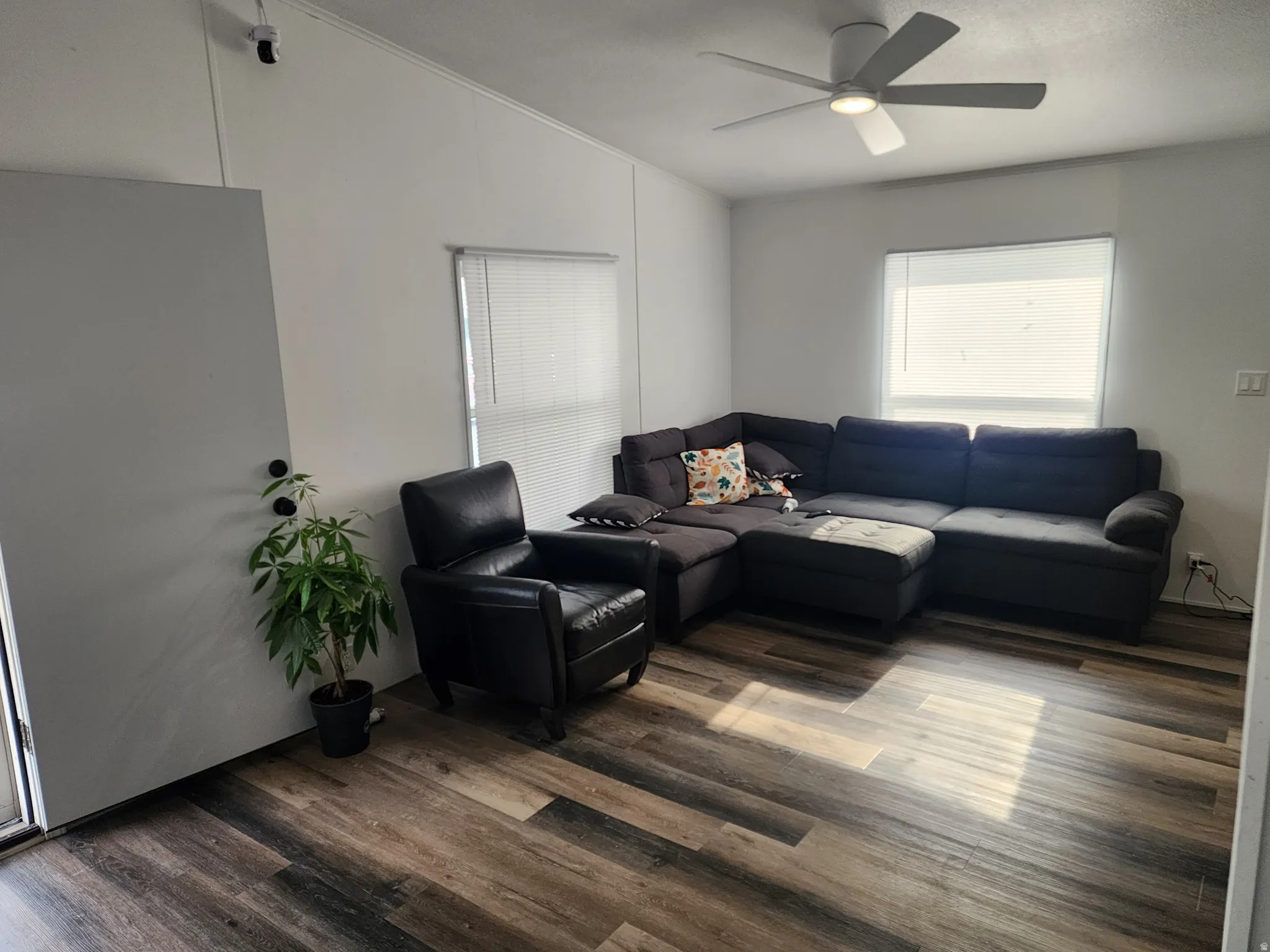 Spacious living area featuring wood-finish flooring, white walls, and a contemporary ceiling fan with integrated lighting