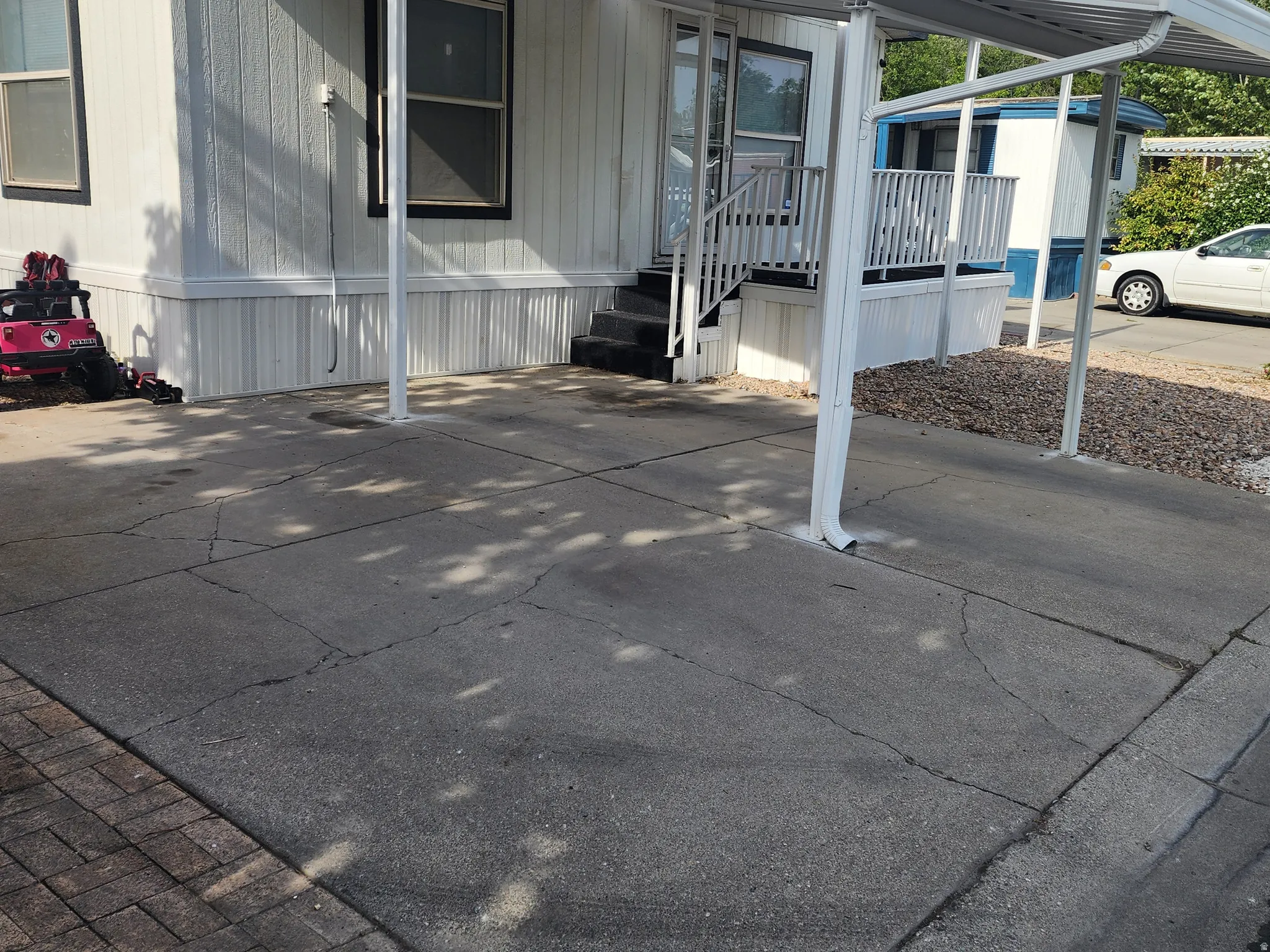 Concrete driveway with carport leading to an entry deck with white railing