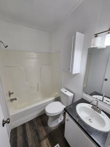 Bathroom featuring a white bathtub and shower surround, wood-finish flooring, and a vanity with a dark countertop and white sink