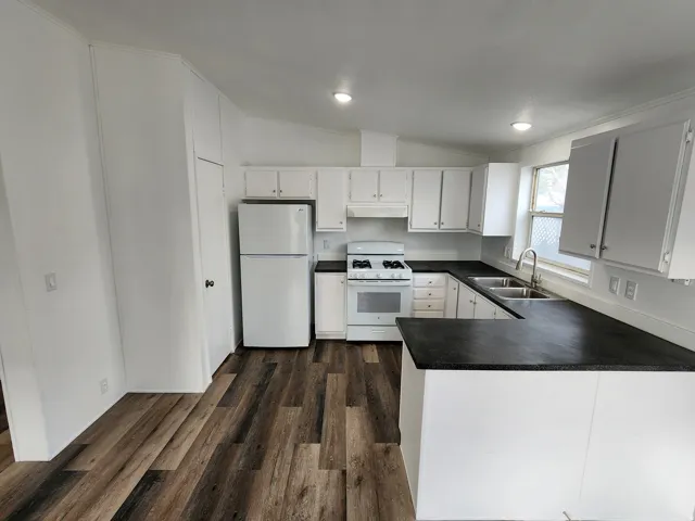Kitchen featuring white cabinetry, dark countertops, a double basin stainless steel sink, wood-finish flooring, and recessed lighting