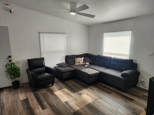 Living area featuring wood-finish flooring, white walls, and a ceiling fan with integrated lighting
