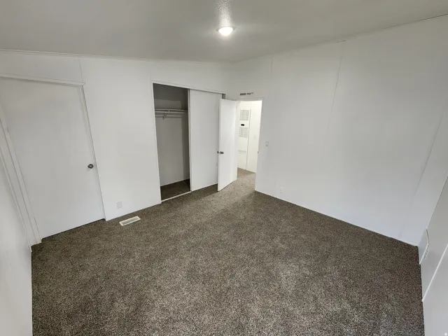Carpeted room featuring white walls, a built-in closet with sliding doors, a white interior door, and an overhead light fixture