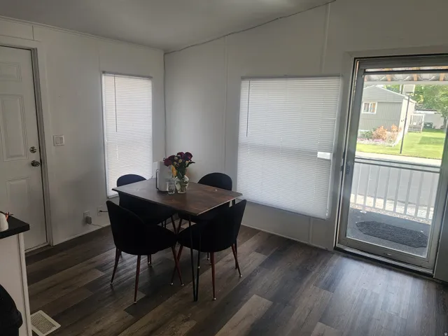 Bright dining area featuring a wood-finish dining table with seating for four, abundant natural light from multiple windows with cellular shades, and sliding glass door access to outdoor space