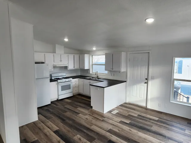 Kitchen featuring white cabinetry, dark countertops, a gas range, and a dual-basin stainless steel sink
