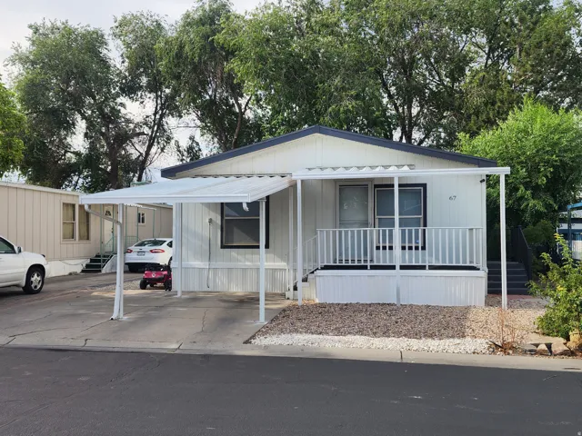 White manufactured home featuring a dark shingled roof, a covered entry porch with white railings, and an attached carport