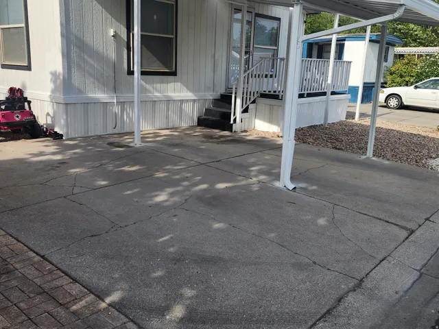 Concrete driveway with carport leading to an entry deck with white railing