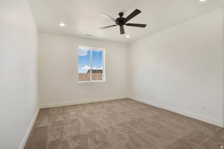 Spacious room featuring neutral carpeting, white walls, and a modern ceiling fan with integrated lighting