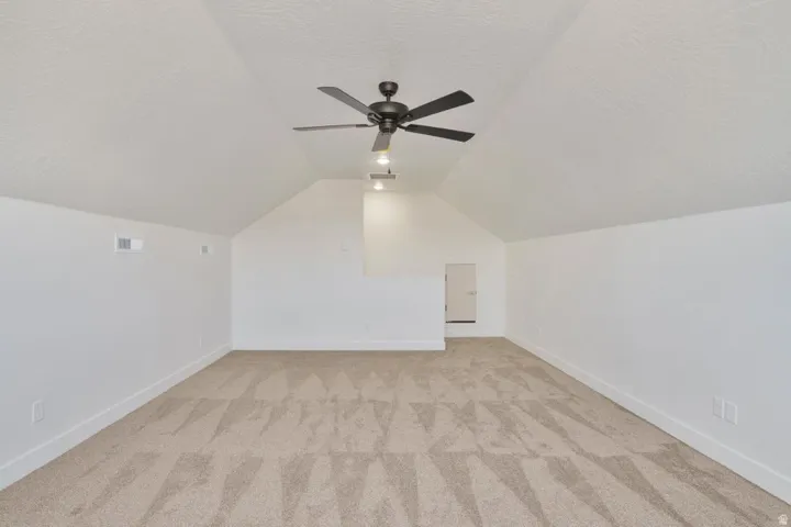 Spacious room featuring vaulted ceilings, a contemporary ceiling fan with integrated lighting, textured neutral carpeting, crisp white walls, and a recessed doorway